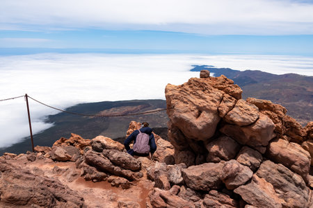 Rear view on hiking woman sitting on rock enjoying panorama from summit of volcano Pico del Teide on the island of Tenerife, Canary Islands, Spain, Europe. Island covered in cloud. Freedom conceptの写真素材