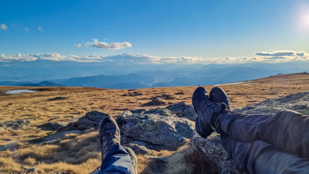 Hiker couple legs resting on alpine meadow with panoramic view on mountains seen from Ladinger Spitz, Saualpe, Lavanttal Alps, Carinthia, Austria, Europe. Trekking in the Austrian Alps on a sunny dayの写真素材