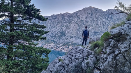 Rear view of man with backpack on rock looking at scenic view near Vrmac Sveti Ilija in summer, Adriatic Mediterranean Sea, Montenegro, Balkans, Europe. Hiking trail in Kotor bay, Dinaric Alpsの写真素材