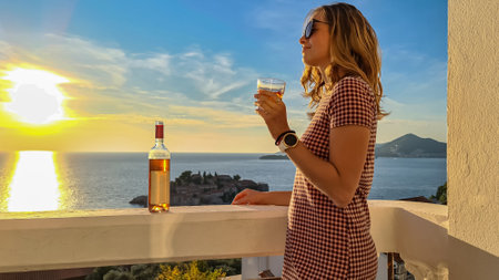 Happy smiling woman drinking wine on balcony in luxury hotel in Budva Riviera with scenic view
