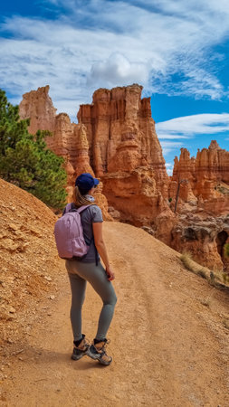 Backpacker woman hiking on Peekaboo trail with scenic view of hoodoo sandstone rock formations in Bryce Canyon National Park, Utah, USA. Pine trees surrounded by natural amphitheatre in sunny summerの写真素材