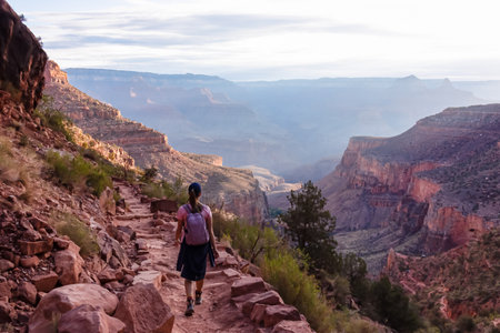Rear view of woman with backpack hiking along Bright Angel trail with panoramic aerial overlook of South Rim of Grand Canyon National Park, Arizona, USA, America. Amazing vista after sunrise in summerの写真素材