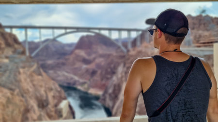 Tourist man wearing hat with scenic view of Mike O'Callaghan Pat Tillman Memorial Bridge near Hoover Dam , Nevada Arizona state line, USA. Historical landmark in Lake Mead National Recreation Areaの写真素材