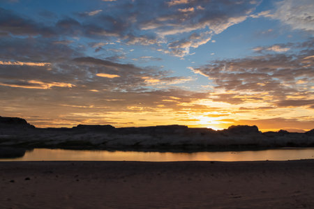 Panoramic sunset view seen from Lone Rock Beach in Wahweap Bay in Lake Powell in Glen Canyon Recreation Area, Page, Utah, USA. Sand beach on wild campground. Red orange sky at sundown, warm atmosphereの写真素材