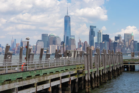 A wooden pier on the Hudson River with captivating New York urban skyline with striking and modern skyscrapers in the back, seen from The Battery Park. Think clouds above the city. Modern city.の写真素材