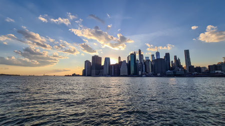Manhattan cityscape at dusk with iconic skyscrapers reflecting on the Hudson River. Great density of skyscrapers, some of them are reflecting the sunbeams of setting sun. Vibrant city.の写真素材