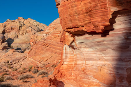 Scenic view on wall of striated red and white rock formations along the White Domes Hiking Trail in Valley of Fire State Park in Mojave desert, Nevada, USA. First sunlight touches arid landscapeの写真素材