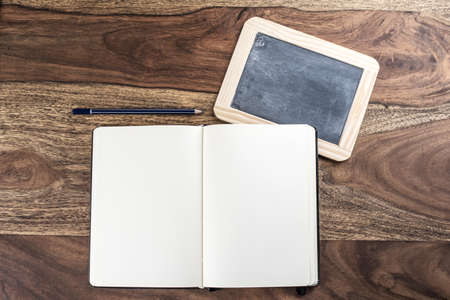 open plain empty page notebook with pencil and blackboard on rustic wood tableの写真素材