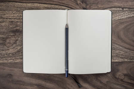 open plain white notebook with pencil on dark wood deskの写真素材