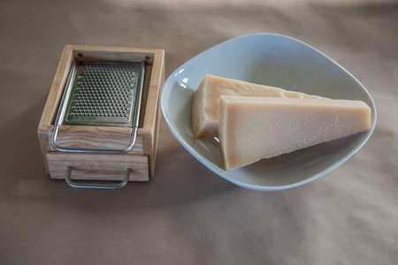pieces of parmesan on a plate besides a wooden cheese graterの写真素材