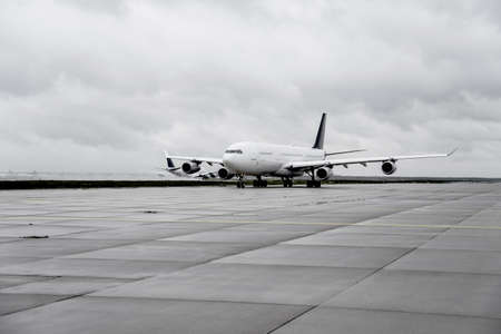airplane on taxiway with another jet taking off on runway in backgroundの写真素材