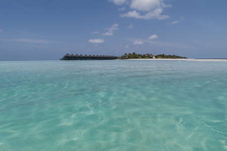 tropical maldives island with palm trees and water houses seen from a sandbank in turquoise waterの写真素材