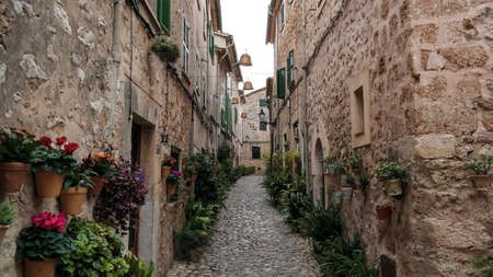 empty narrow street in Valldemossa Mallorca with typical historic houses on both sides and mountains in far distant backgroundの写真素材
