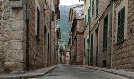 low angle shot of empty narrow street in Soller Mallorca with typical historic houses on both sides and mountains in far distant backgroundの写真素材