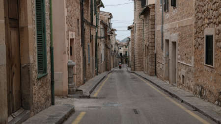 motorcyclist riding down empty narrow street in Soller Mallorca with typical historic houses on both sides and mountains in far distant backgroundの写真素材