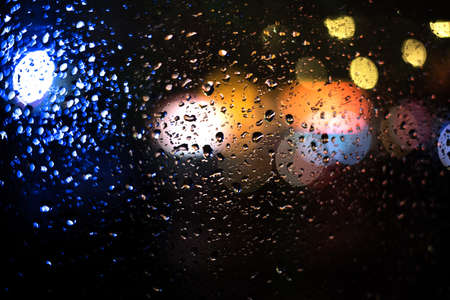 drops of water on glass window with bokeh traffic lights in dark backgroundの写真素材