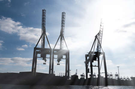 silhouettes of large harbor cranes against blue sky backlit