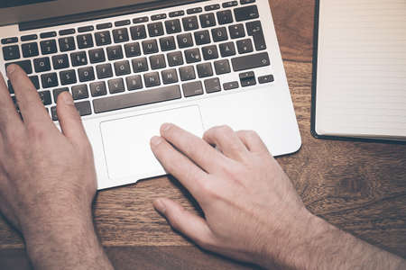 top view of the hands of a male person wirking on a notebook computer on a rustic wooden desktopの写真素材