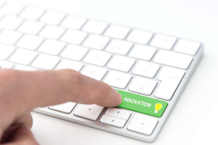finger pressing a green key labeled INNOVATION with glowing light bulb symbol on a computer keyboardの写真素材