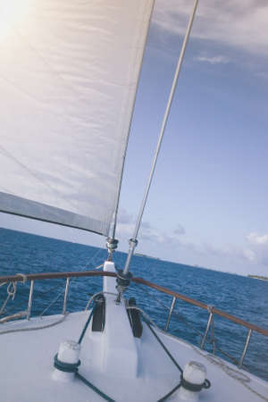 bow of a sailboat in deep blue water under blue sky with small tropical islands on distant horizonの写真素材