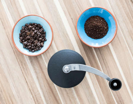 top view of manual coffee grinder and two bowls with coffee beans and ground coffee on wooden surfaceの写真素材