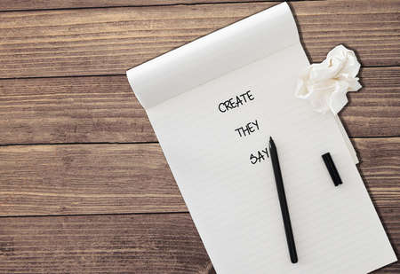 ruled notepad with words CREATE THEY SAY with black felt tip pen and a piece of crumpled paper isolated on rustic wooden table backgroundの写真素材