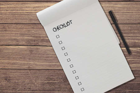 top view of blank ruled notepad with chicklist and pen side by side on rustic wooden table...