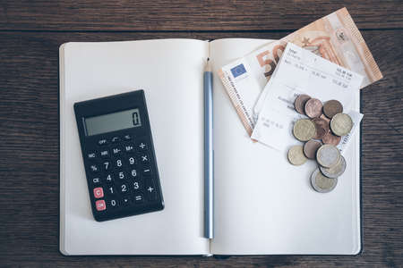 account book concept with cash bills and coins, notebook and calculator on rusitc wooden tableの写真素材