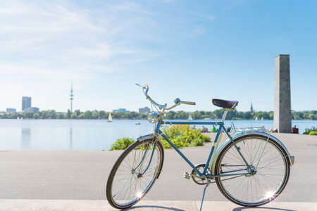 vintage blue bicycle parked at lakeshore of Alster Lake in Hamburg, Germany under beautiful clear blue summer sky with cityscape in blurred backgroundの写真素材