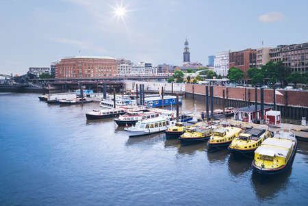 excursion boats in Hamburg harbor near Baumwall station with steeple of Sankt Michaelis church in backgroundの写真素材