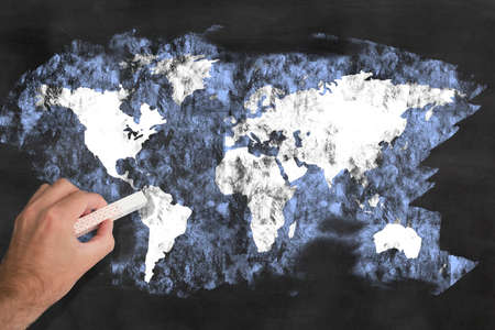 hand holding a piece of chalk drawing a map of the world on a blackboardの写真素材