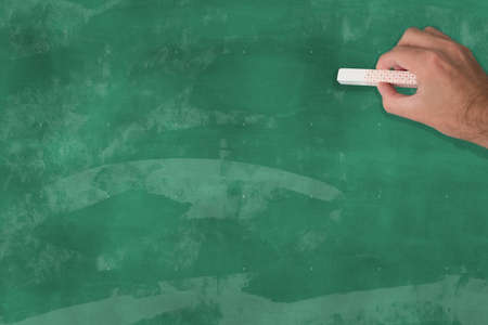 hand holding a piece of chalk in front of a blank chalkboardの写真素材