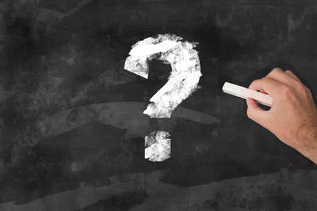 hand with a piece of chalk drawing a question mark on a chalkboardの写真素材