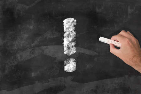 hand with a piece of chalk drawing an exclamation mark on a chalkboardの写真素材