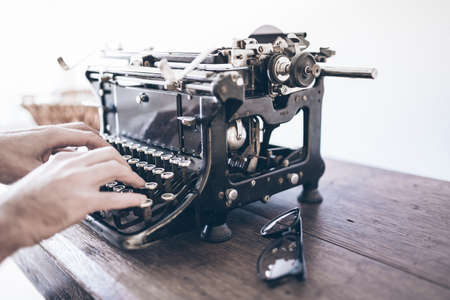 close-up of man using vintage manual typewriter on rustic wooden tableの写真素材