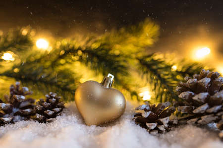 snowy winter christmas decoration with heart shaped christmas ornament, cones, fir branch and glowing lightsの写真素材