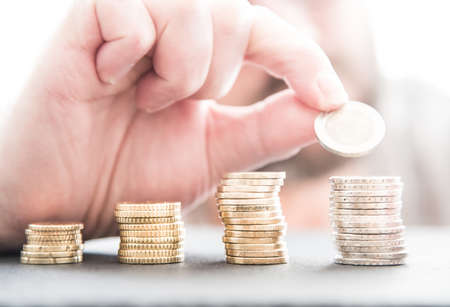 hand piling up stacks of euro coins on light grey stone surface with bright background