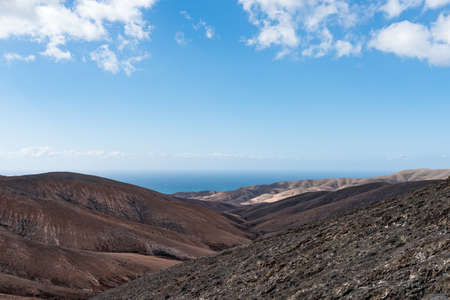 arid rolling landscape with ocean in background under blue sky on Fuerteventura islandの写真素材
