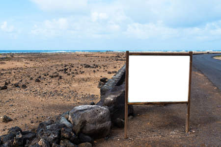 blank white empty sign post, billboard, information board, sign at roadside in deserted coastal landscape with ocean in backgroundの写真素材