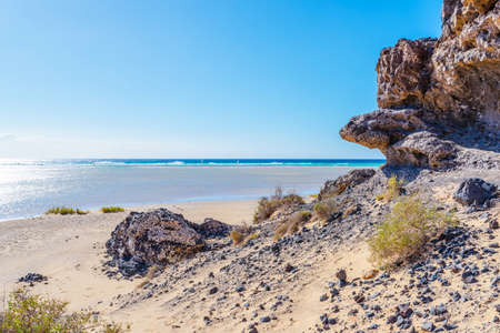 rock formation on empty sand beach against blue ocean and sky on Fuerteventura island on sunny dayの写真素材