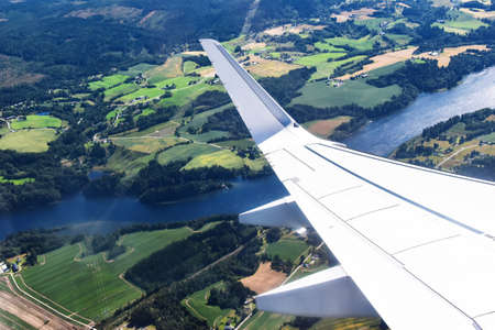 wing of a commercial plane against rural landscape with river during take-off or landingの写真素材
