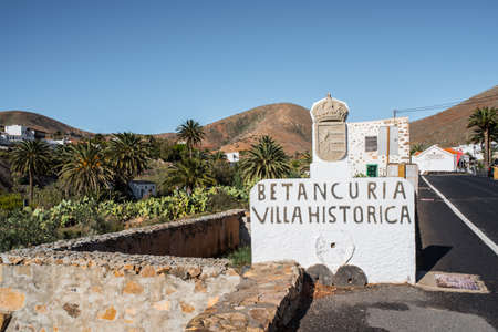 01-29-2018 Betancuria, Fuerteventura, Spain: historic town sign in Betancuria with village and mountain range in background against blue skyのeditorial素材