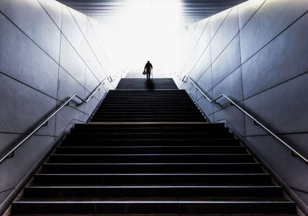 silhouette of senior man with a walking stick carrying shopping bags up a long flight of stairsの写真素材