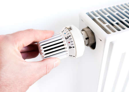 hand of man adjusting temperature on thermostat on radiatorの写真素材