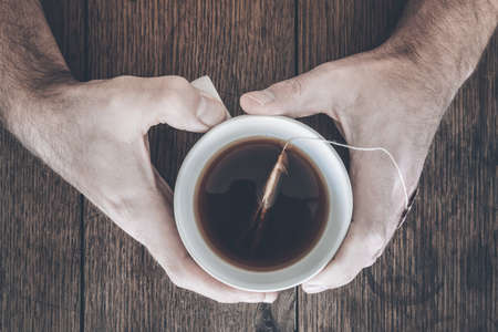 hands holding cup of steaming hot tea on old rustic wooden tableの写真素材