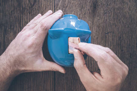 top view of hands of male person putting money into piggy bank savings conceptの写真素材