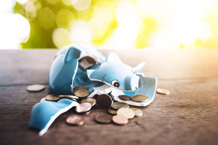 closeup of shattered broken piggy bank with coins on rustic wooden table finance conceptの写真素材