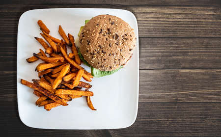 top view of plate with burger and sweet potato fries on rustic wooden tableの写真素材