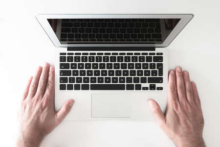 top view of both hands of man placed besides notebook computer on white desk