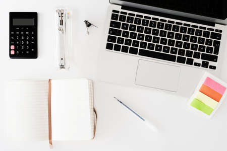 overhead view of white desk with notebook, calculator, note pad and office suppliesの写真素材